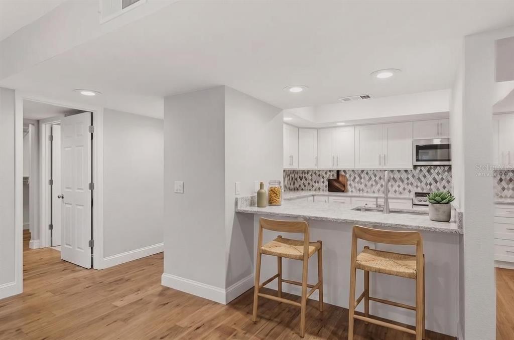 A kitchen with white cabinets, granite countertops, and a breakfast bar with two wooden stools — 125 MARINER DRIVE UNIT 125, TARPON SPRINGS, FL