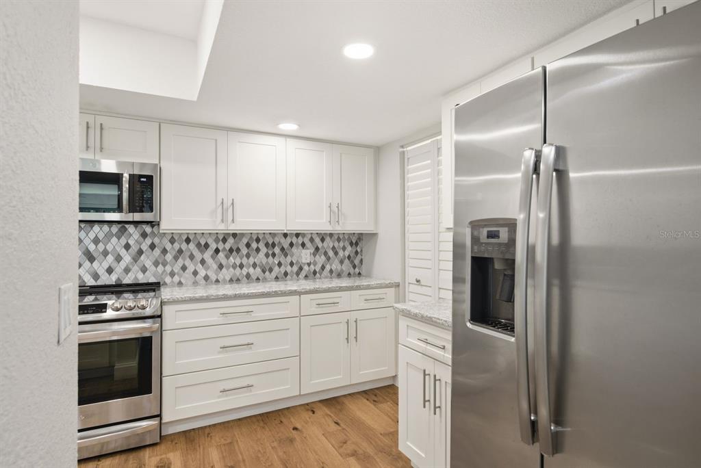 A kitchen features white cabinets, stainless steel appliances, a patterned backsplash, and wood-look flooring — 125 MARINER DRIVE UNIT 125, TARPON SPRINGS, FL
