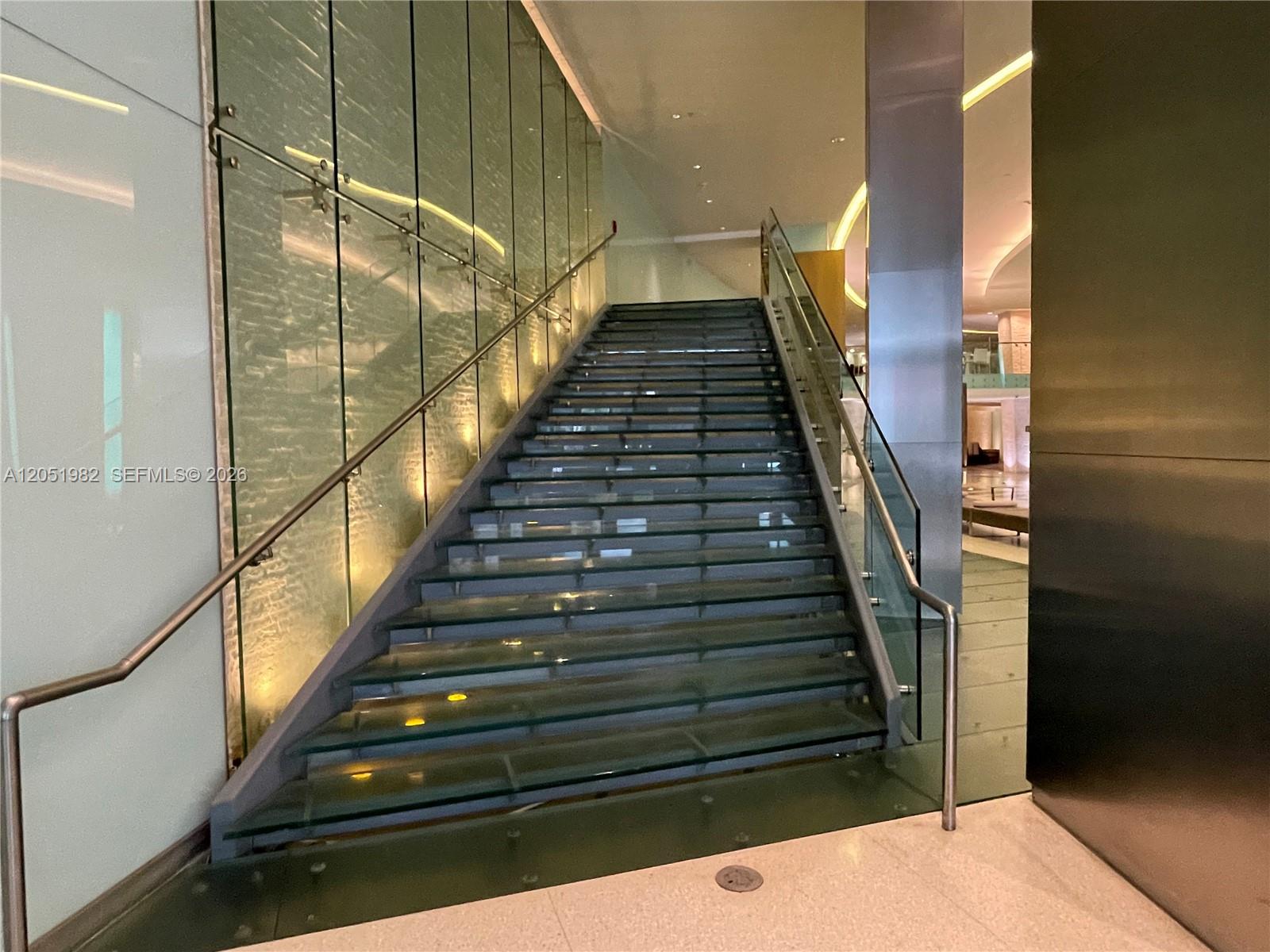 A modern staircase with glass steps and railings ascends between a glass wall and pillar — 92 SW 3rd St # 5012, Miami FL 33130, MIAMI, FL