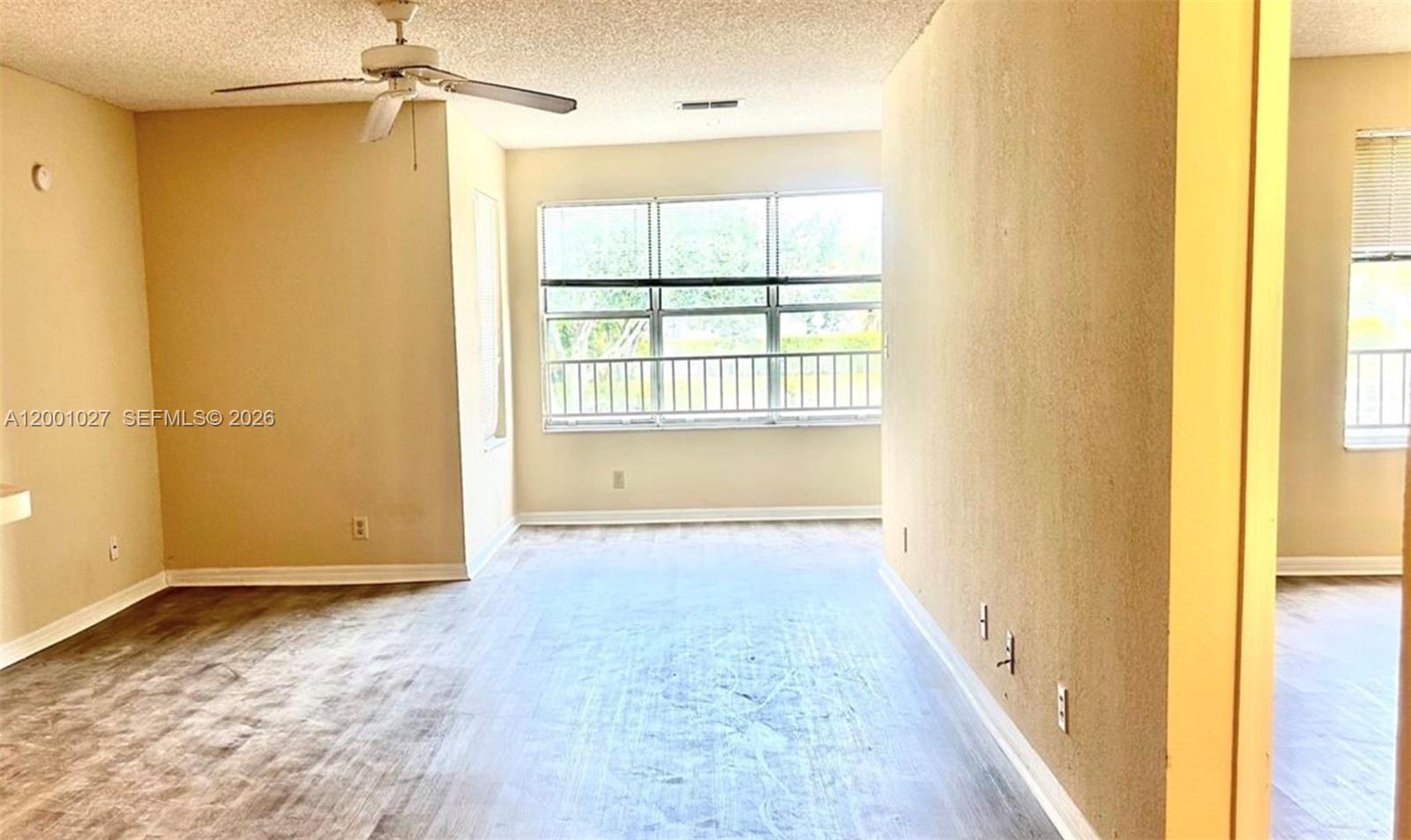 An empty room features light-colored walls, wood-look flooring, a ceiling fan, and large windows — 3310 N Pinewalk Dr N # 1823, Margate FL 33063, MARGATE, FL