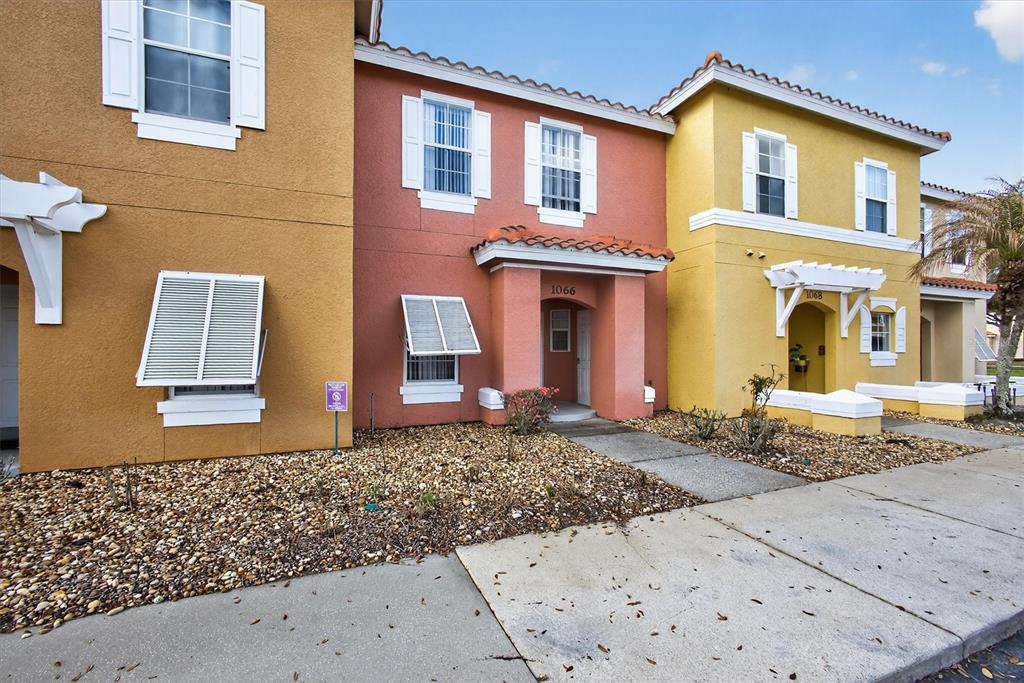 The exterior of three attached townhomes features stucco walls in yellow and orange — 1066 PARK RIDGE CIRCLE, KISSIMMEE, FL