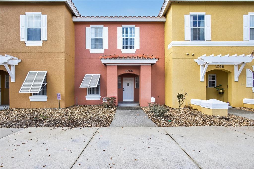 The exterior of a multi-story townhouse complex features tan, coral, and yellow stucco facades — 1066 PARK RIDGE CIRCLE, KISSIMMEE, FL