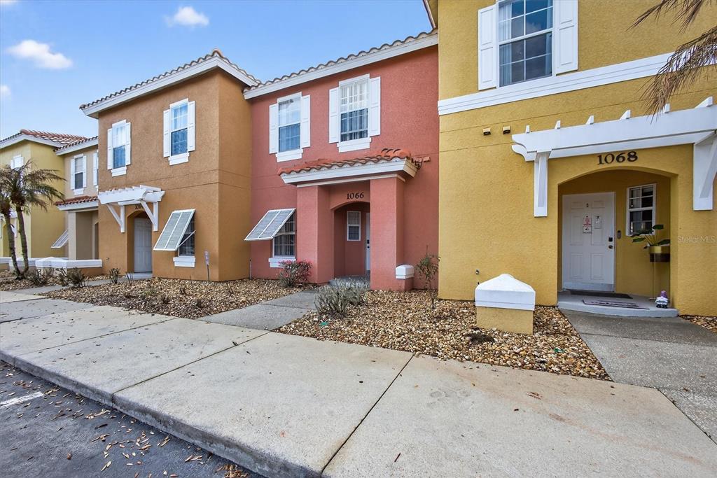 A row of colorful townhouses with stucco exteriors, white shutters, and gravel landscaping — 1066 PARK RIDGE CIRCLE, KISSIMMEE, FL