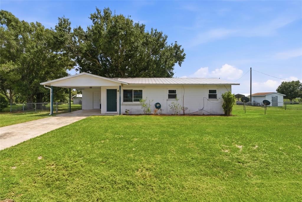 A single-story white house with a metal roof, carport, and a large front lawn — 1597 SE TANGELO DRIVE, ARCADIA, FL