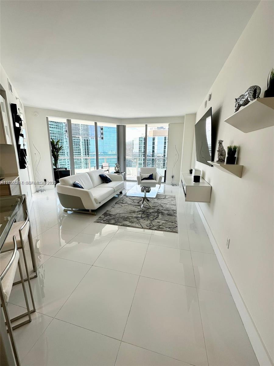 A modern living room features white tile floors, a white sofa, and floor-to-ceiling windows — 1300 Brickell Bay Dr # 3101, Miami FL 33131, MIAMI, FL