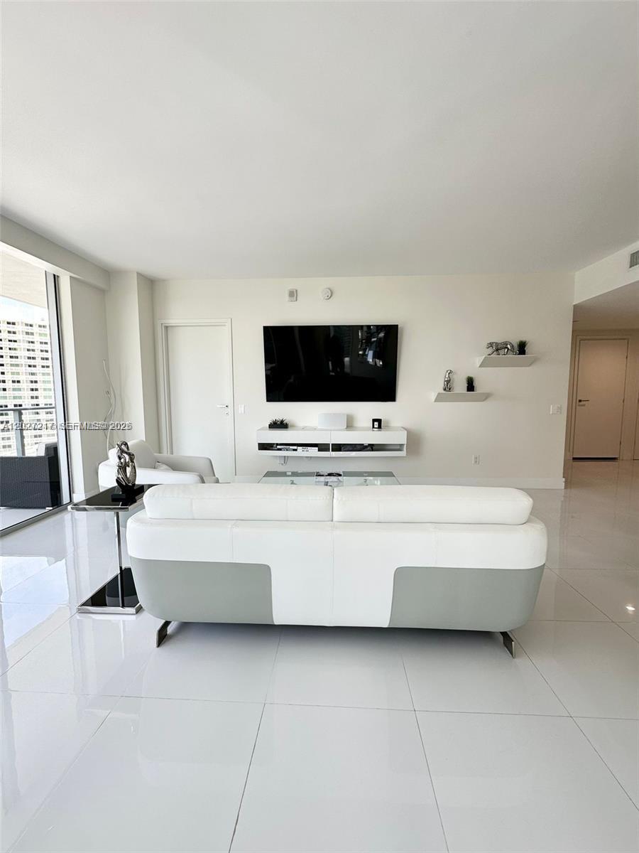 A modern living room features a white sofa, a wall-mounted television, and glossy tile flooring — 1300 Brickell Bay Dr # 3101, Miami FL 33131, MIAMI, FL