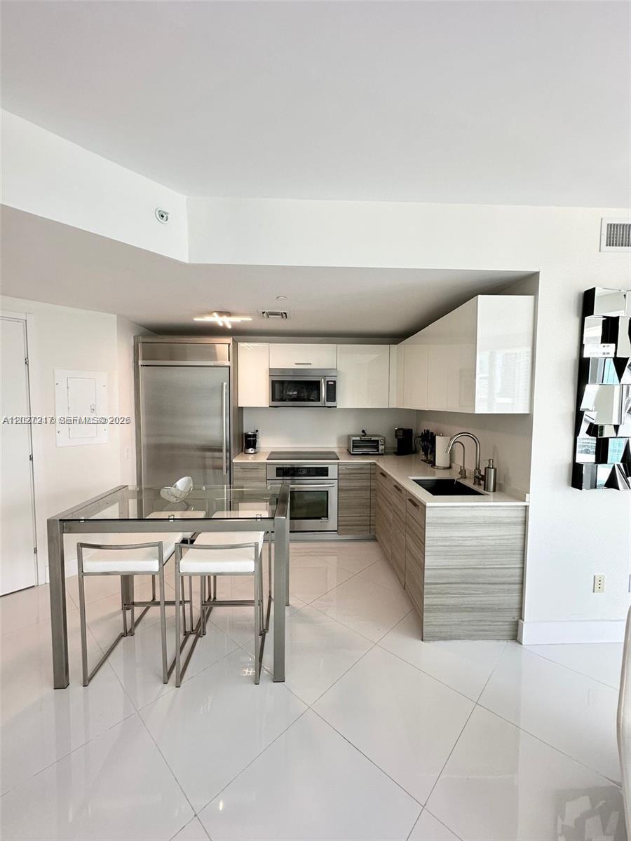 A modern kitchen features white upper cabinets, wood-grain lower cabinets, stainless steel appliances, and tile flooring — 1300 Brickell Bay Dr # 3101, Miami FL 33131, MIAMI, FL