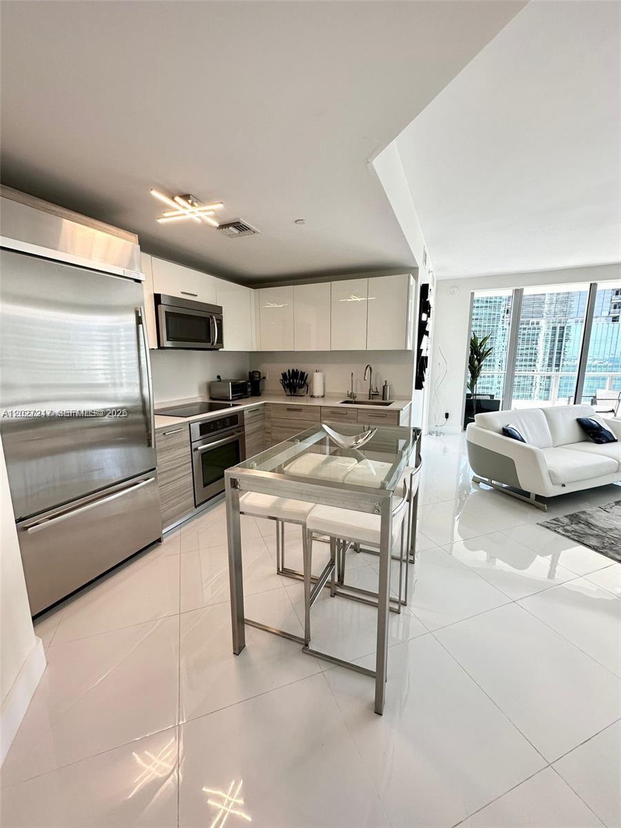 A modern kitchen with white cabinetry and stainless steel appliances opens to a living area — 1300 Brickell Bay Dr # 3101, Miami FL 33131, MIAMI, FL
