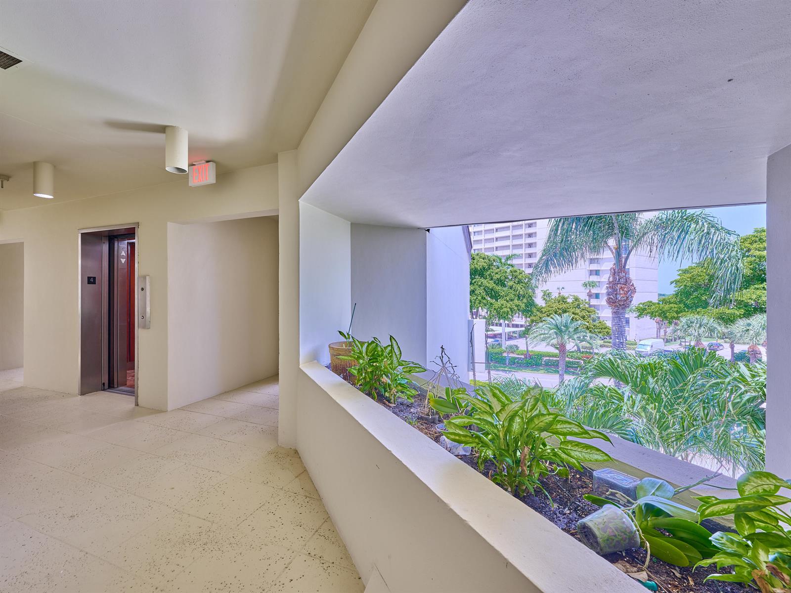 An indoor hallway features an elevator, tiled floors, and a planter box overlooking tropical landscaping — 1117 Marine Way E, North Palm Beach FL 33408, NORTH PALM BEACH, FL