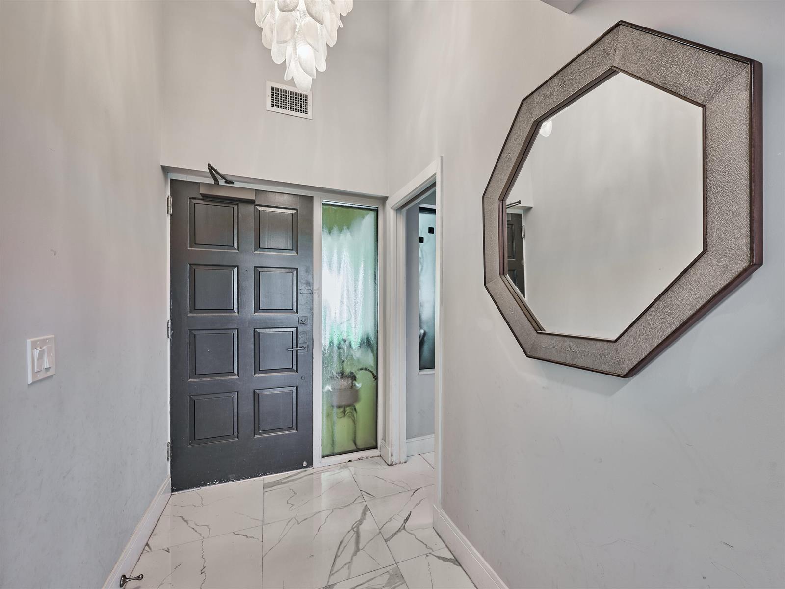An entryway features a dark front door, marble-look tile flooring, and a large octagonal mirror — 1117 Marine Way E, North Palm Beach FL 33408, NORTH PALM BEACH, FL