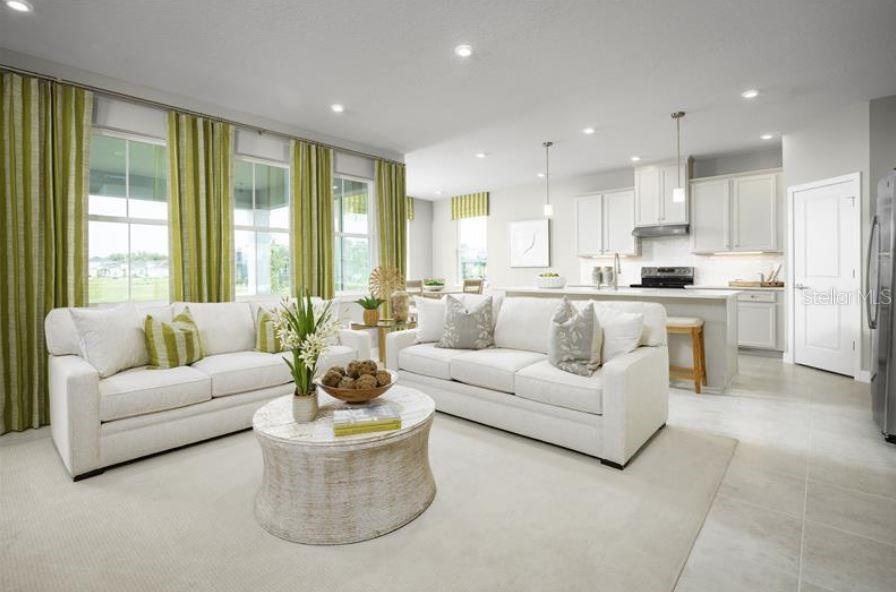 A bright, open-concept living room and kitchen featuring white sofas, green curtains, and light-colored flooring — 22141 PINE GROVE LOOP, LEESBURG, FL