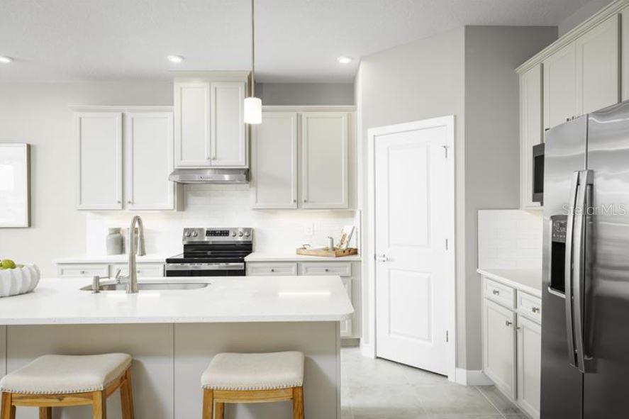 A modern kitchen features white cabinetry, a large island with bar seating, and stainless steel appliances — 22141 PINE GROVE LOOP, LEESBURG, FL