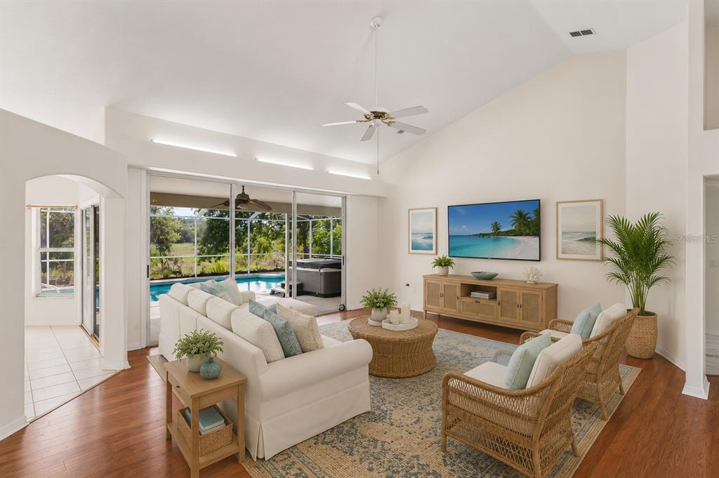 A living room with a vaulted ceiling, white sofa, wicker furniture, and a pool view — 6381 PINEHURST DRIVE, SPRING HILL, FL
