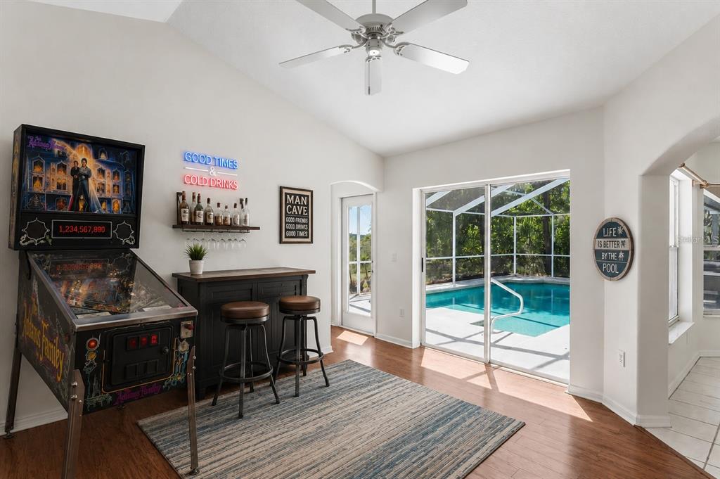 A room with a pinball machine, a small bar, and sliding doors opening to a pool — 6381 PINEHURST DRIVE, SPRING HILL, FL