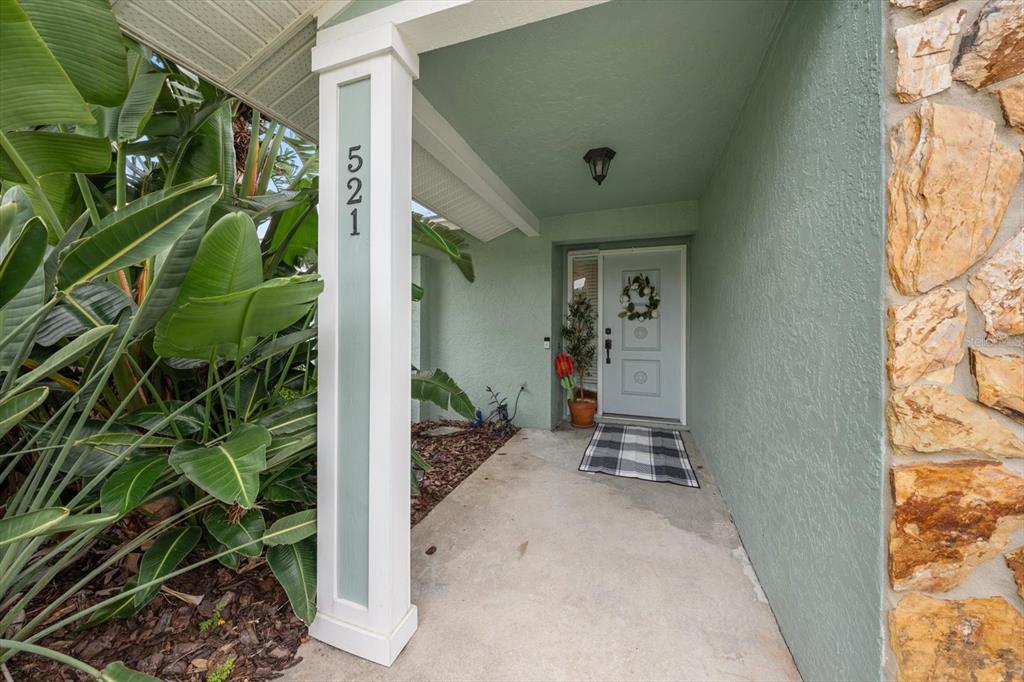 A covered entryway features a light green exterior, a white support pillar, and a front door — 521 MERAVAN DRIVE, PALM HARBOR, FL