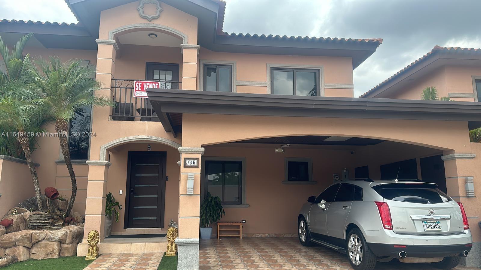 A two-story house with a tan stucco exterior, a covered carport, and a silver SUV — 56-D Versalles I - Panama City, PA Panama, PA