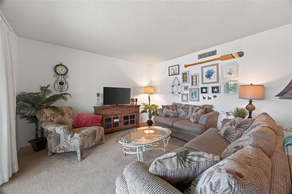 A living room features a beige carpet, patterned furniture, a glass coffee table, and wall decor — 569 MIDWAY DRIVE UNIT B, OCALA, FL