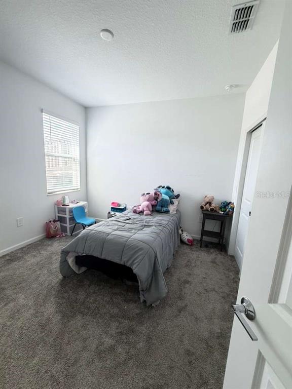 A bedroom features gray carpet, a single bed with a gray comforter, and a window — 1103 POMELO STREET, DAVENPORT, FL