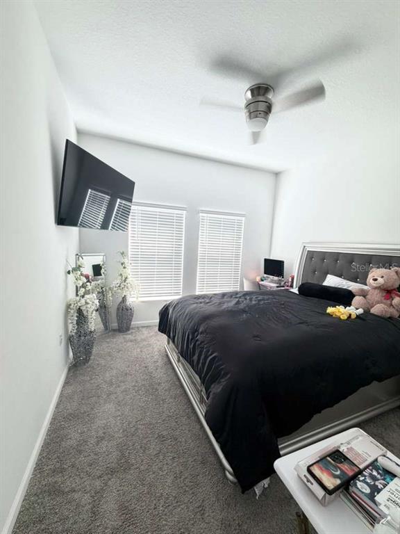 A bedroom features a bed with a black comforter, gray carpeting, and a wall-mounted television — 1103 POMELO STREET, DAVENPORT, FL