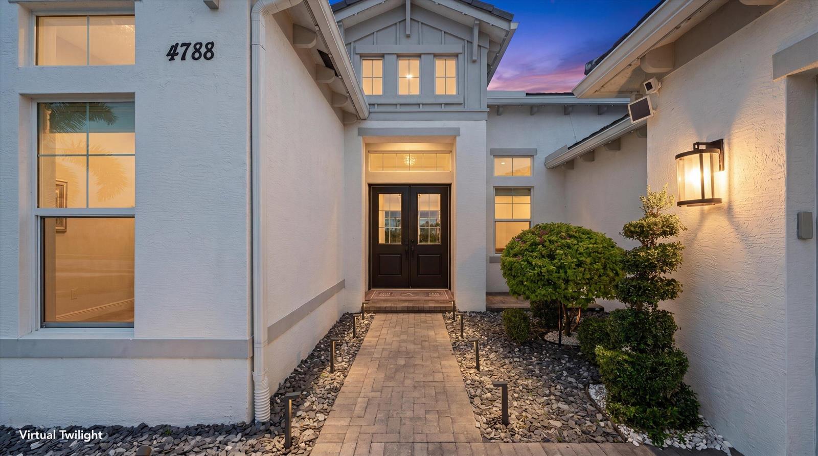 A paved walkway leads to the dark double front doors of a white stucco house — 4788 Estates Circle, Westlake FL 33470, WESTLAKE, FL