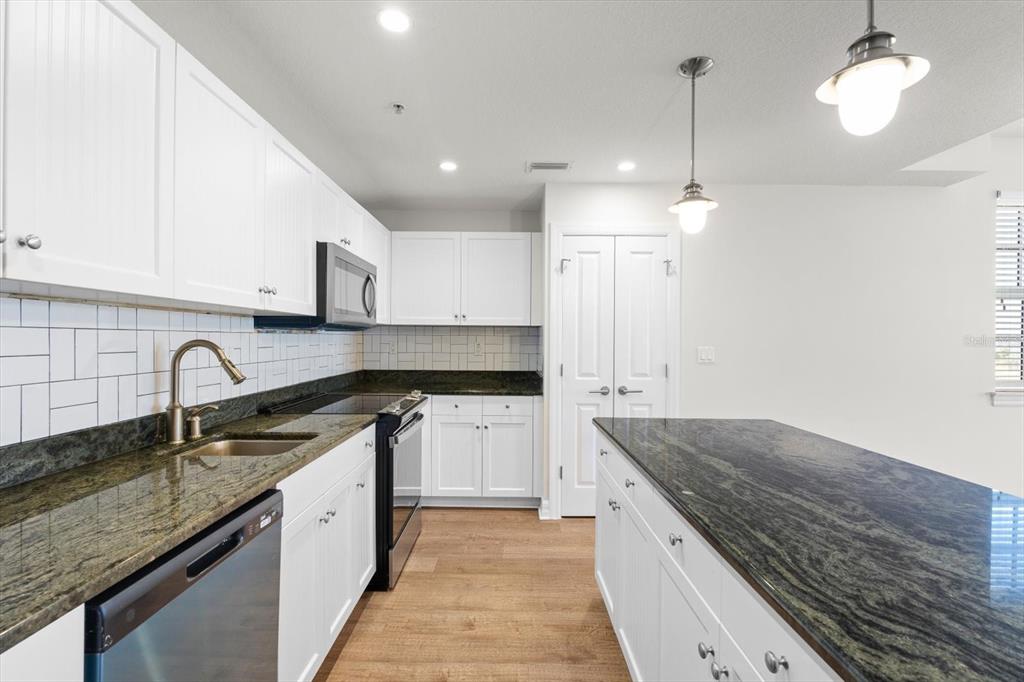 A kitchen with white cabinets, dark granite countertops, stainless steel appliances, and wood-look flooring — 536 BAHIA BEACH BOULEVARD UNIT 236C, RUSKIN, FL