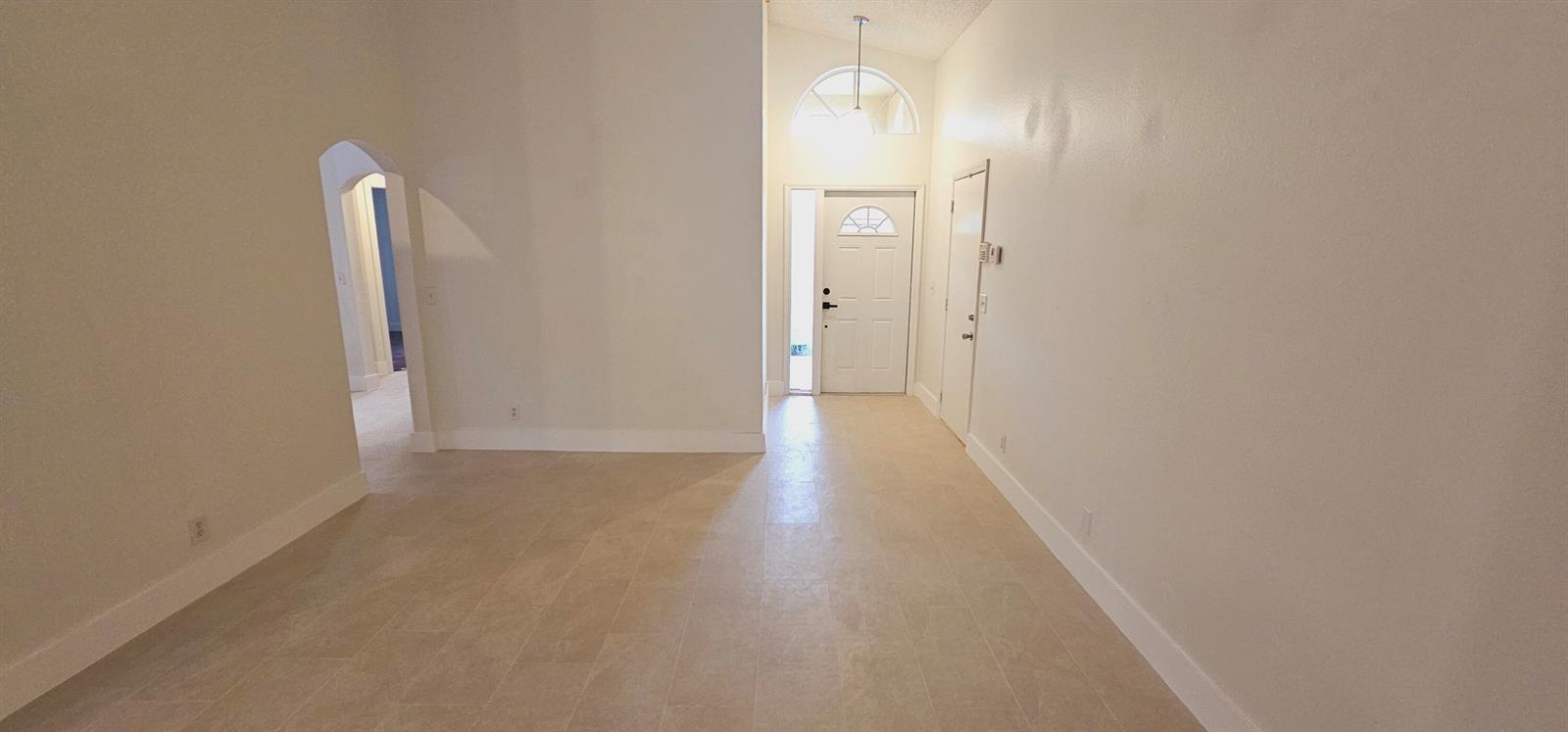 An empty room with light-colored tile flooring, white walls, and an arched entryway — 10780 Cypress Lake Terrace, Boca Raton FL 33498, BOCA RATON, FL