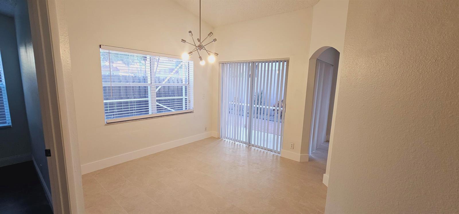 An empty dining room features tile flooring, a modern chandelier, and sliding glass patio doors — 10780 Cypress Lake Terrace, Boca Raton FL 33498, BOCA RATON, FL