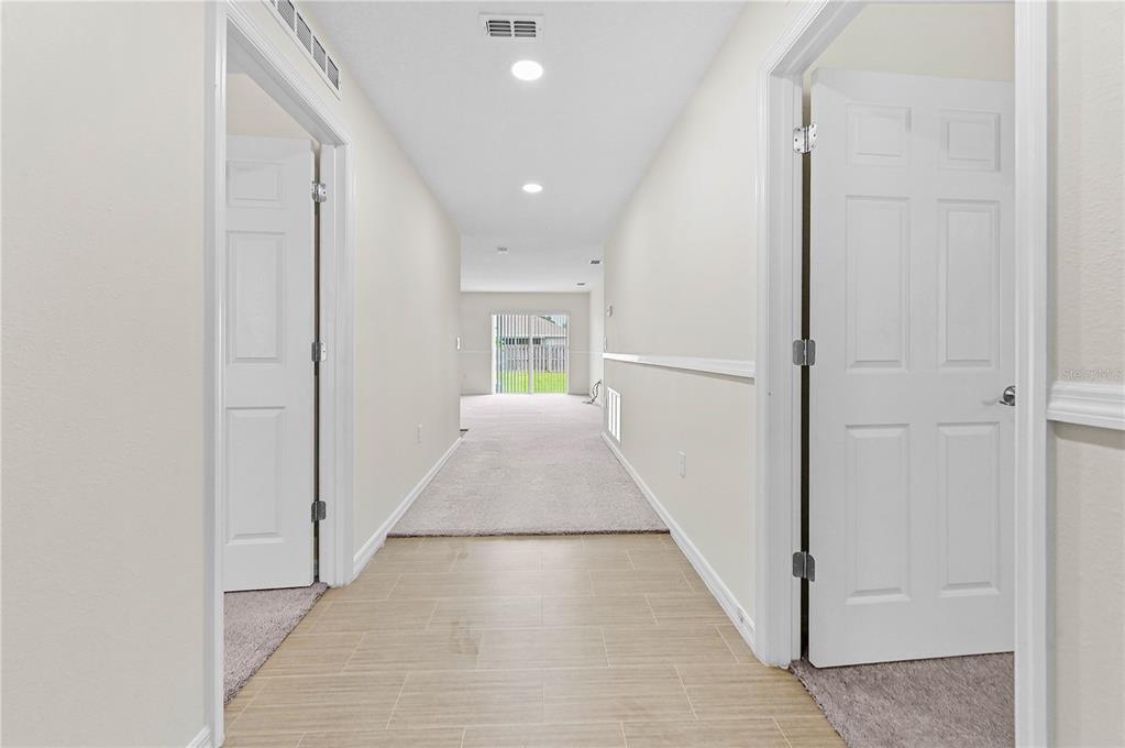 A hallway with tile flooring leads to a carpeted living area with sliding glass doors — 361 SW THORNHILL DRIVE, PORT ST LUCIE, FL