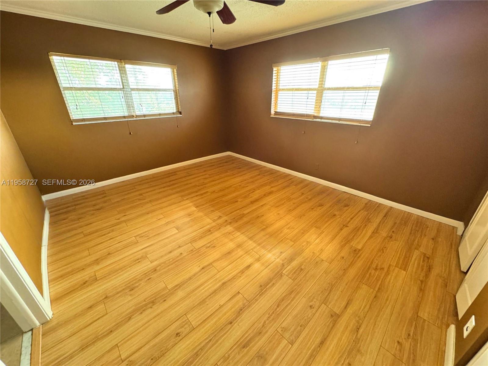 An empty bedroom features brown walls, light wood-look flooring, and two windows with blinds — 2060 NW 48th Ter # 308, Lauderhill FL 33313, LAUDERHILL, FL