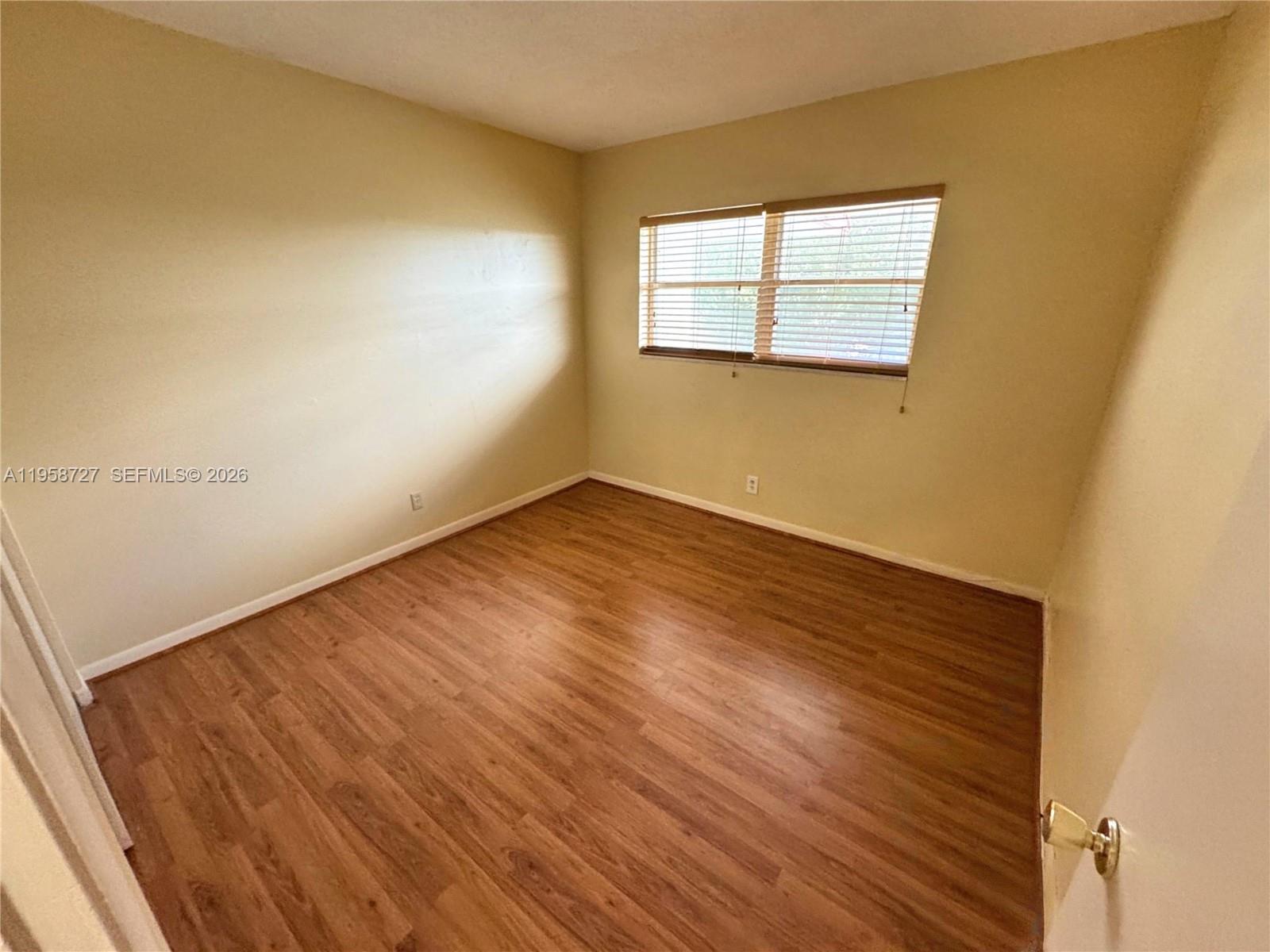 An empty bedroom features light-colored walls, wood-look flooring, and a window with blinds — 2060 NW 48th Ter # 308, Lauderhill FL 33313, LAUDERHILL, FL