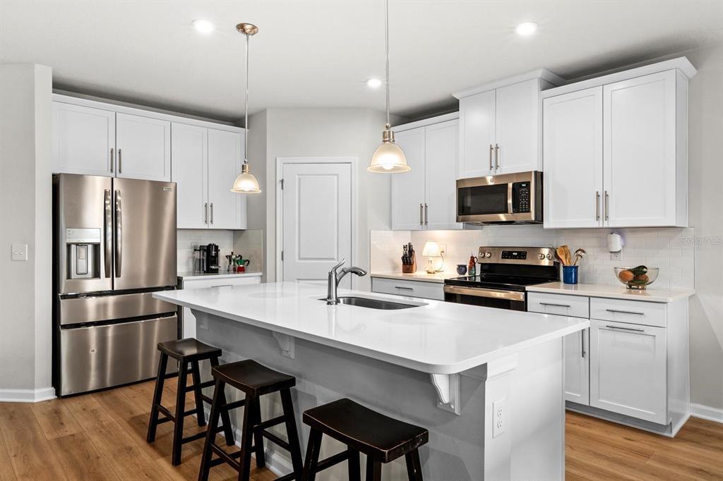 A modern kitchen features white cabinetry, stainless steel appliances, and a large central island — 10024 EVENTIDE TRAIL, PARRISH, FL