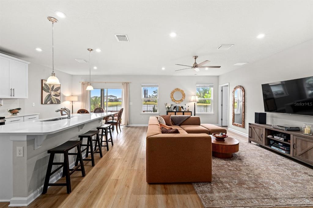 An open-concept kitchen and living room with a large island, brown sofa, and wood flooring — 10024 EVENTIDE TRAIL, PARRISH, FL