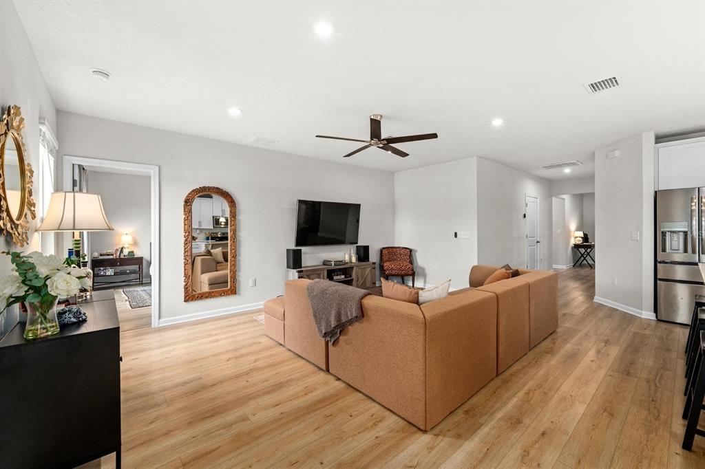 A living room features light wood flooring, a brown sectional sofa, and a ceiling fan — 10024 EVENTIDE TRAIL, PARRISH, FL
