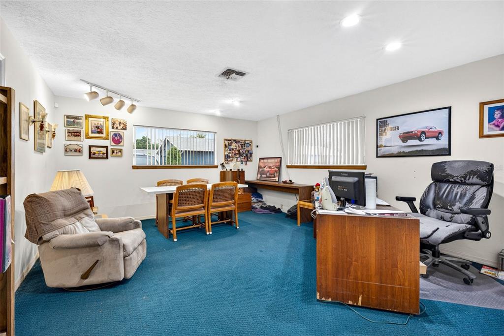 A room with blue carpeting, a desk, a dining table, and wall-mounted car posters — 10221 US HIGHWAY 301, DADE CITY, FL