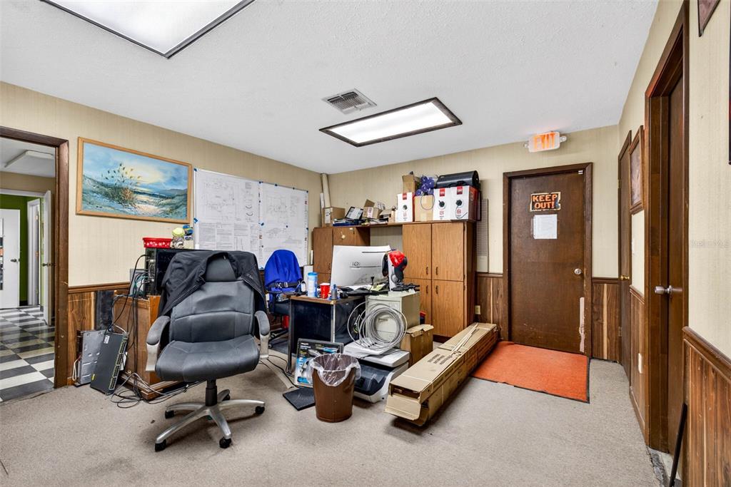 A cluttered office space features wood-paneled walls, a desk with a chair, and storage cabinets — 10221 US HIGHWAY 301, DADE CITY, FL