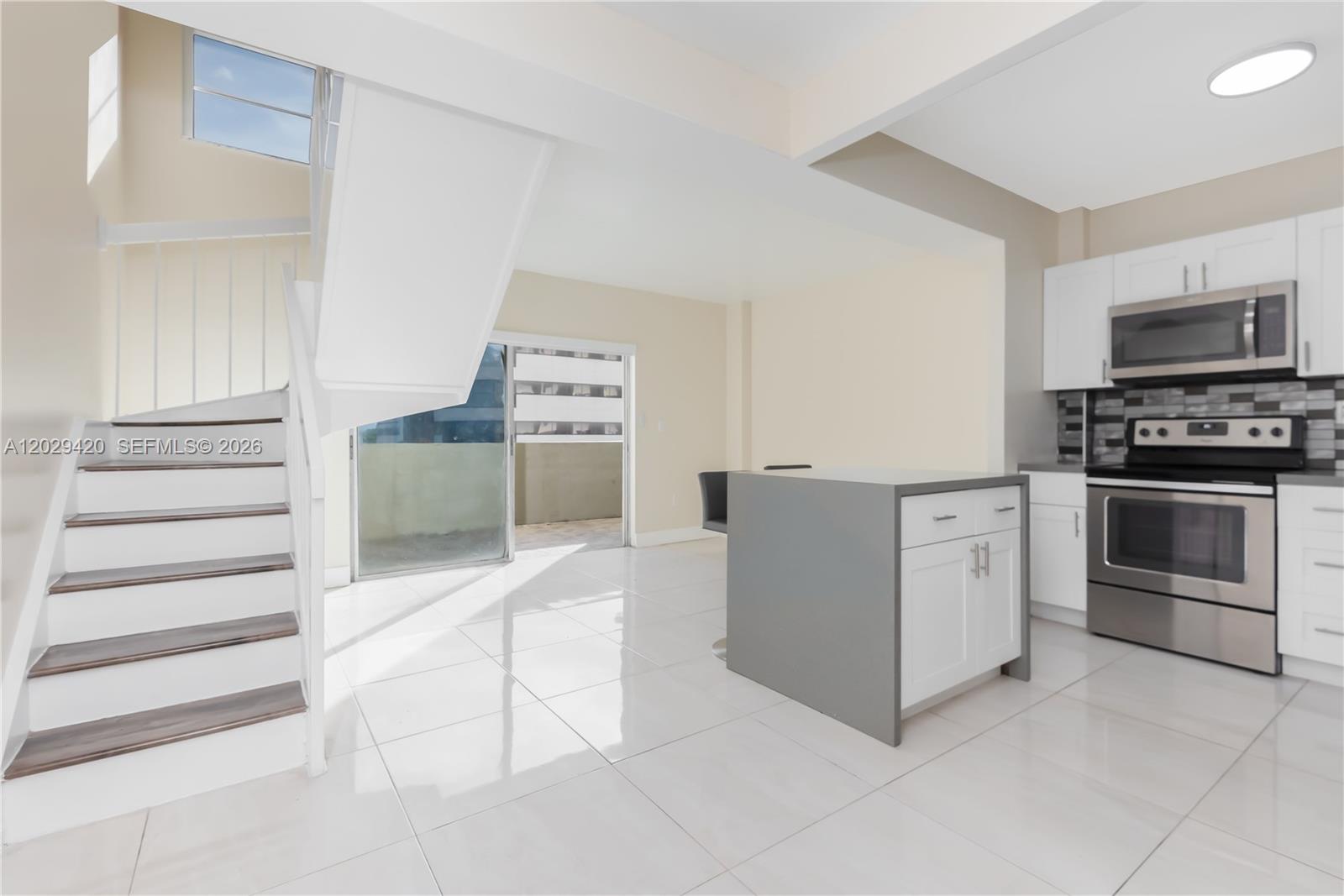 A modern kitchen with white cabinets, stainless appliances, and a staircase leading to a loft — 300 NW 42nd Ave # 411, Miami FL 33126, MIAMI, FL