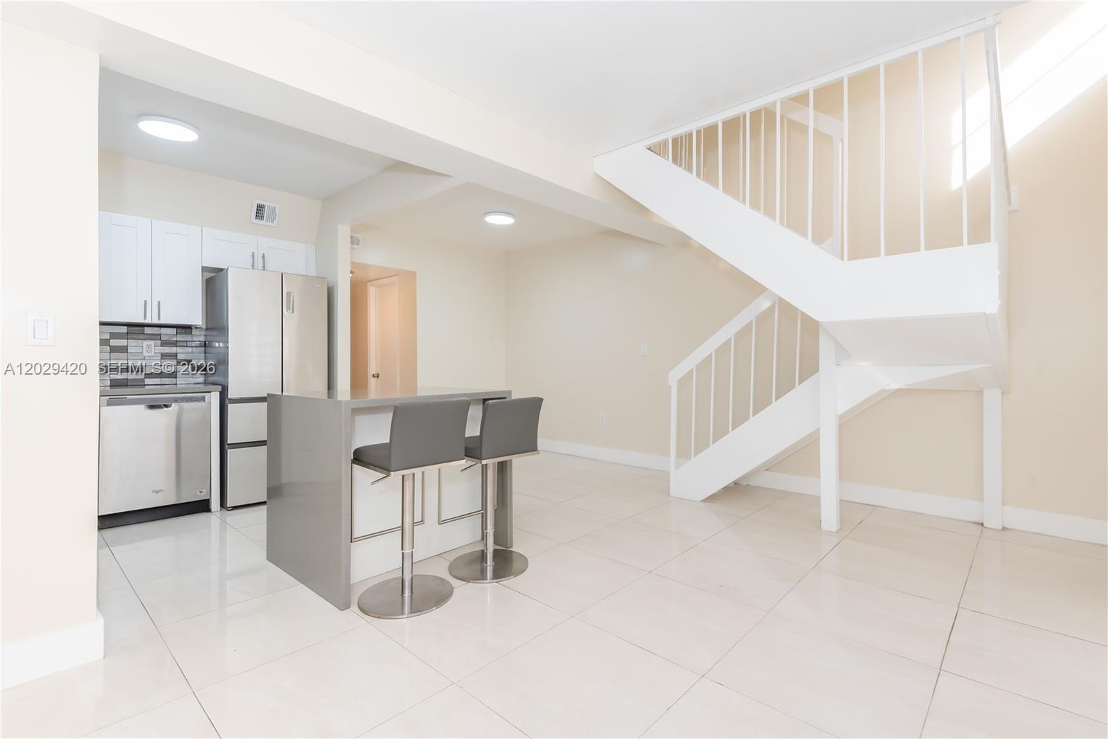 A kitchen with white cabinets and a gray island sits beside a white staircase — 300 NW 42nd Ave # 411, Miami FL 33126, MIAMI, FL