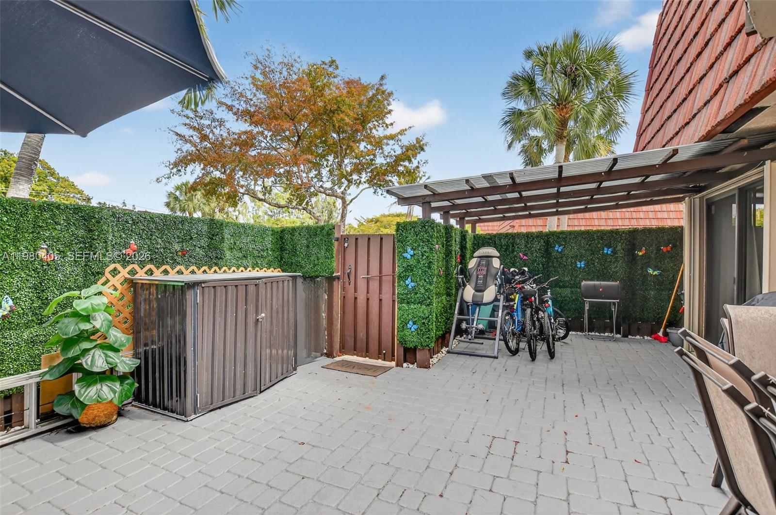 A paved patio features a storage shed, bicycles, an inversion table, and artificial hedge fencing — 8181 Boca Rio Dr # 8181, Boca Raton FL 33433, BOCA RATON, FL