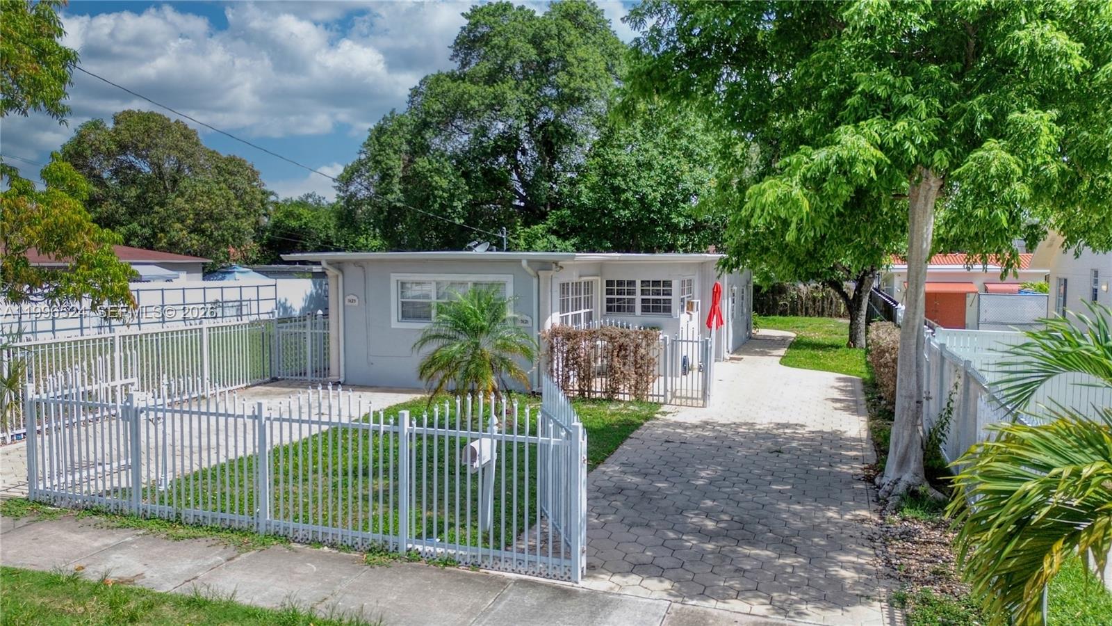 A single-story gray house with a paved driveway and white metal fencing in the front — 3121-3123 SW 25th Ter, Miami FL 33133, MIAMI, FL
