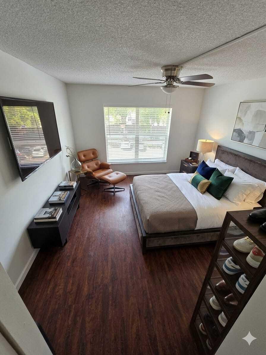 A bedroom features dark wood flooring, a bed with decorative pillows, and a leather lounge chair — 3670 Inverrary Drive # 3y, Lauderhill FL 33319, LAUDERHILL, FL