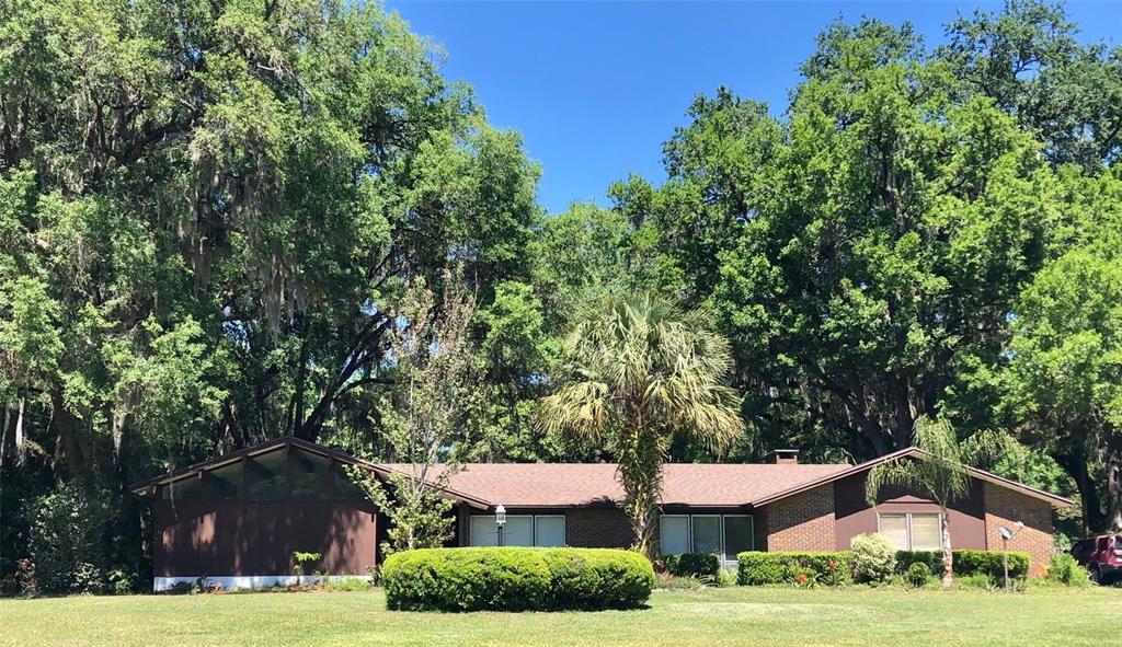 A single-story brick house with a gabled roof sits on a lawn surrounded by trees — 8136 NW 5TH COURT, GAINESVILLE, FL