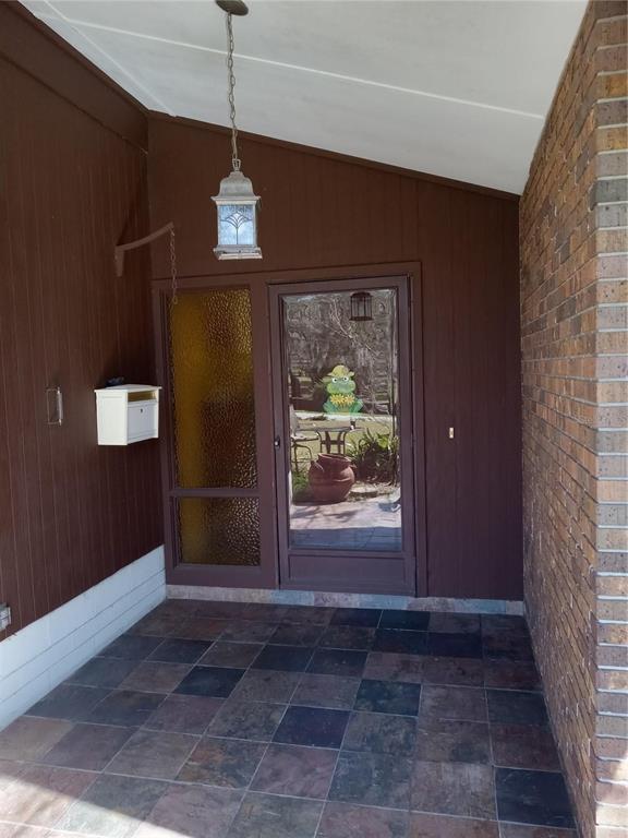 A covered porch features brown wood siding, a brick wall, tiled flooring, and a glass door — 8136 NW 5TH COURT, GAINESVILLE, FL