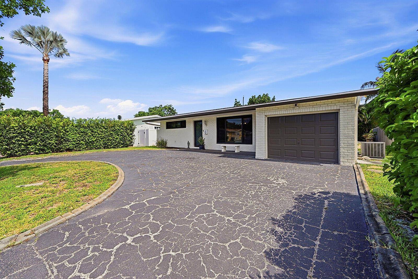 A single-story white brick house features a dark garage door and a cracked asphalt driveway — 8370 NW 26th Place, Sunrise FL 33322, SUNRISE, FL