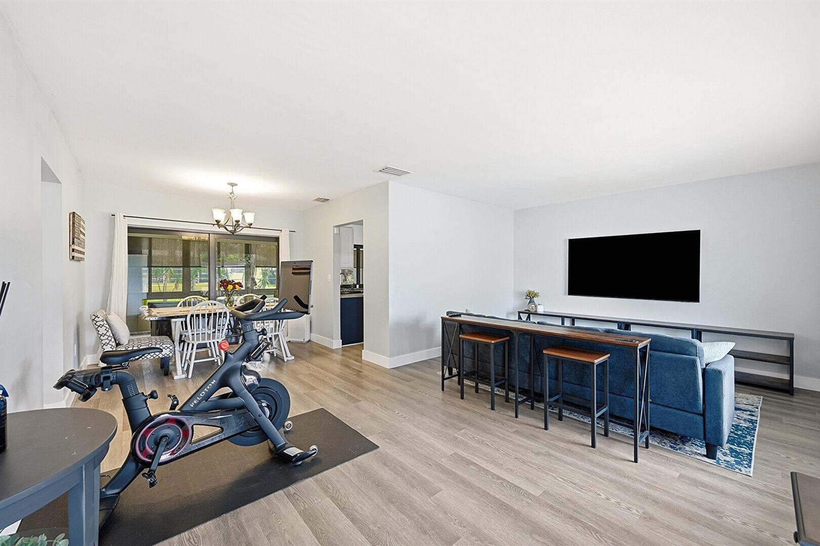 A living and dining room features light wood flooring, a Peloton bike, and blue sofa — 8370 NW 26th Place, Sunrise FL 33322, SUNRISE, FL