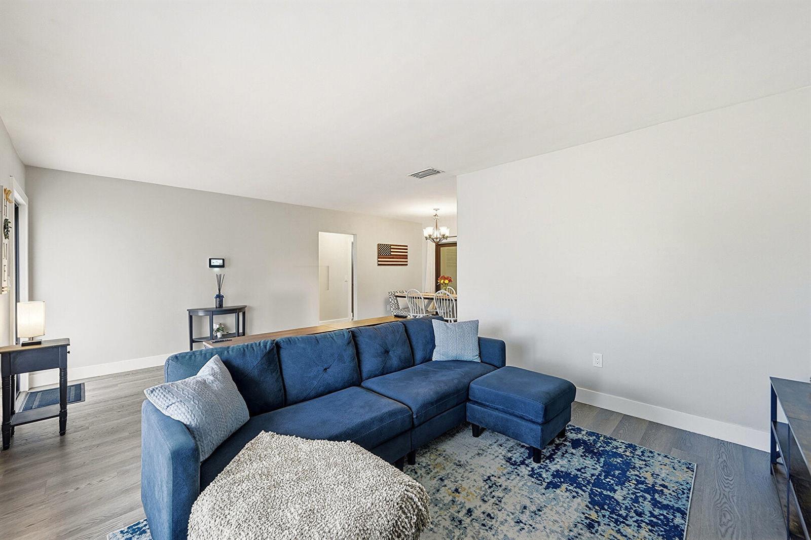 A living room features a blue sectional sofa, a patterned rug, and light wood flooring — 8370 NW 26th Place, Sunrise FL 33322, SUNRISE, FL