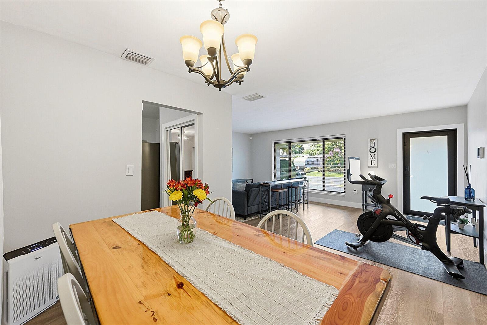 A dining area with a wooden table and chandelier opens into a living room with exercise equipment — 8370 NW 26th Place, Sunrise FL 33322, SUNRISE, FL