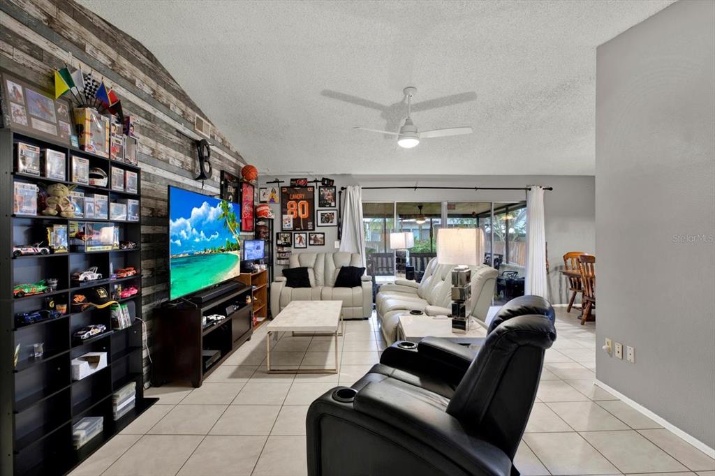 A living room features a wood-paneled accent wall, a large television, and tile flooring — 7604 S SANIBEL DRIVE, TAMPA, FL