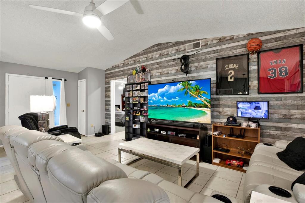 A living room features a wood-paneled accent wall, a large television, and a white sofa — 7604 S SANIBEL DRIVE, TAMPA, FL
