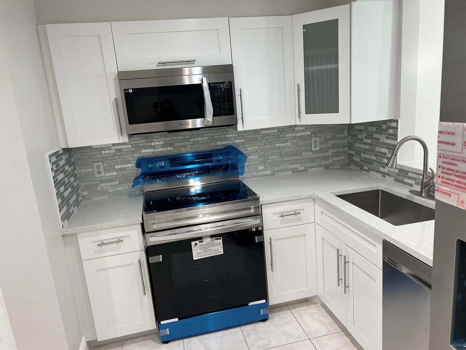 A modern kitchen features white cabinets, stainless steel appliances, a tiled backsplash, and quartz countertops — 24 Abbey Lane # 204, Delray Beach FL 33446, DELRAY BEACH, FL