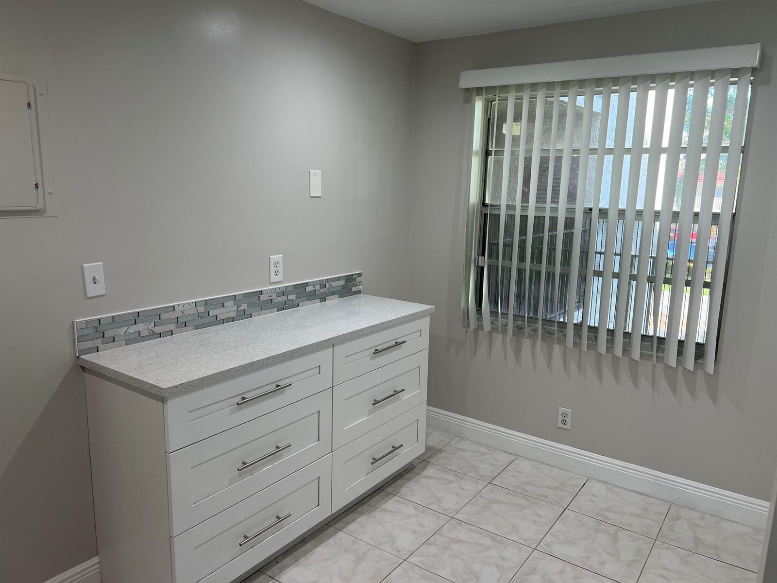 A room with white cabinets, a speckled countertop, a tiled backsplash, and a window — 24 Abbey Lane # 204, Delray Beach FL 33446, DELRAY BEACH, FL